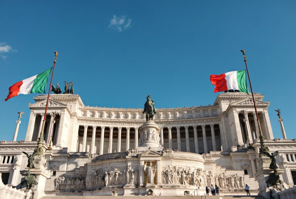 Bâtiment italien blanc, drapeaux italiens et statues sous un ciel bleu pendant la journée